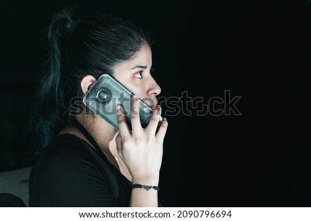 beautiful latina woman with green hair receiving an extortion call, with her cell phone in her hand. with her gaze upwards and serious look. with a black background. concept of technology and robbery.