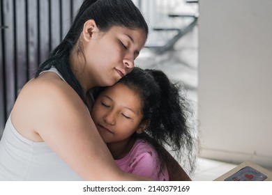 beautiful latina woman hugging her brown-skinned daughter, feeling proud and happy to have her by the side. little girl next to her mother giving the a hug with her eyes closed.