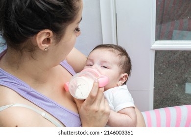 beautiful latina woman looking at her two month old baby as she feeds her and she starts to fall asleep in her arms. tender baby with her eyes half closed about to fall asleep. concept of motherhood.