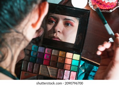Beautiful latina woman looking in the mirror of her eye shadow palette, with her gaze fixed on her eyes, girl making up her eyes with red eyeshadow. beauty concept