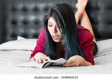 beautiful latina woman reading a book lying on her bed, with an expression of amazement. the girl is very impressed with the new offerings of her fashion magazine. - Powered by Shutterstock