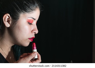 beautiful latina woman using a brush to paint her lips red, girl with her eyes painted with red shadow. with space for advertising text. black background. beauty concept.