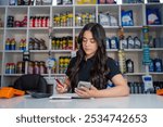 Beautiful Latina woman working holding air filter and looking at smartphone in auto parts store