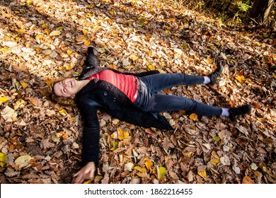 Beautiful laughing woman, lying on a carpet of fallen leaves and making "snow angel" in a lush autumn foliage in the forest. Relaxing and having fun in the woods. Motion blur.