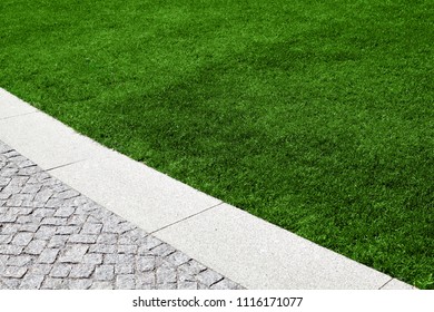 A Beautiful Lawn With Green Grass And A Path Decorated With Granite Stones.