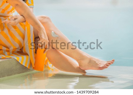 Beautiful Legs with Sunscreen. Woman apply sun protection cream on her legs. Skincare. Sun cream on Feet and  holding a plastic orange package sunscreen bottle sitting near pool. Copy space