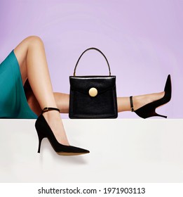 Beautiful legs woman with black heels shoes and purse on purple background.	
