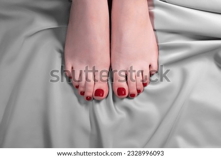 Beautiful legs of a young girl with a red pedicure on a background of gray silk fabric.  The concept of skin care and hardware manicure, nail service master, beauty salon