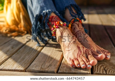 Beautiful legs of young woman wearing jeans, beads accessories and with mehendi over wooden desk background