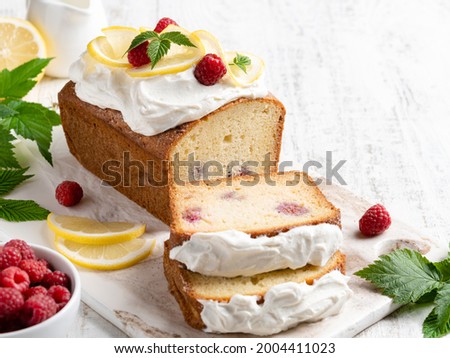 Beautiful lemon raspberry cake with cream cheese frosting and festive decoration sliced and served with fresh berries, lemon slices. Summer dessert. Pound cake on white wooden background.  Copy space.