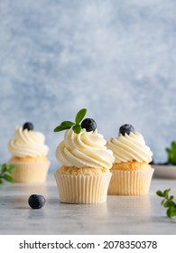 Beautiful lemon vanilla cupcakes with cream cheese frosting decorated with fresh blueberries and green leaves. Delicious homemade dessert. Festive bakery. Blue background. Copy space. Close up food.