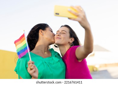 A Beautiful Lesbian Young Couple Embraces And Holds A Rainbow Flag. Girls Taking Selfie Photo