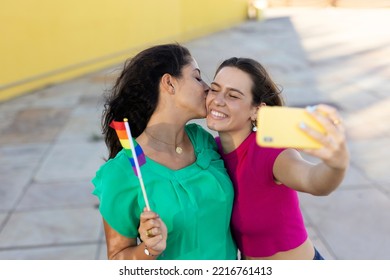 A Beautiful Lesbian Young Couple Embraces And Holds A Rainbow Flag. Girls Taking Selfie Photo