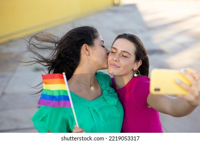 A Beautiful Lesbian Young Couple Embraces And Holds A Rainbow Flag. Girls Taking Selfie Photo	