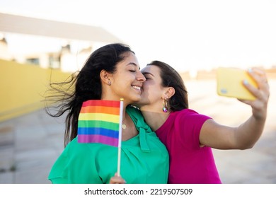 A Beautiful Lesbian Young Couple Embraces And Holds A Rainbow Flag. Girls Taking Selfie Photo.