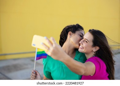 A Beautiful Lesbian Young Couple Embraces And Holds A Rainbow Flag. Girls Taking Selfie Photo.