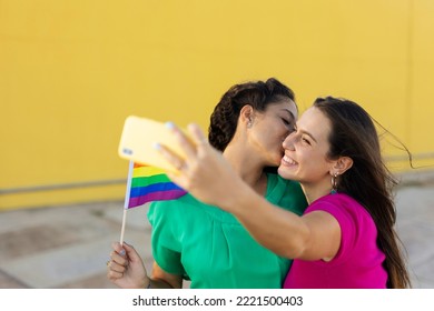 A Beautiful Lesbian Young Couple Embraces And Holds A Rainbow Flag. Girls Taking Selfie Photo