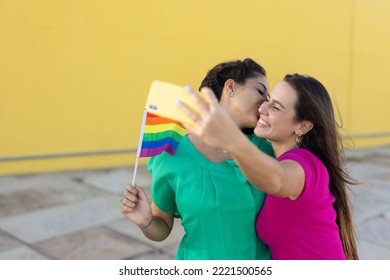 A Beautiful Lesbian Young Couple Embraces And Holds A Rainbow Flag. Girls Taking Selfie Photo