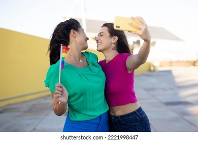 A Beautiful Lesbian Young Couple Embraces And Holds A Rainbow Flag. Girls Taking Selfie Photo.	