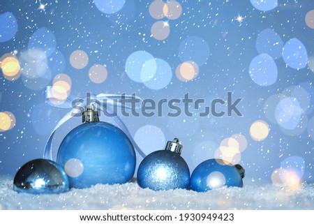 Beautiful light blue Christmas balls on snow against blurred festive lights, bokeh effect. Space for text