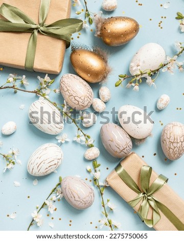 beautiful light easter layout with eco-wrapped gifts, golden and marble eggs, cherry blossoms and confetti on a pastel blue background. top view. copy space. flat lay. place for text