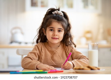 Beautiful Little Arab Girl Sitting At Table In Kitchen And Drawing, Cute Female Kid Painting With Pencils At Home, Enjoying Preschooler Development Activities And Looking At Camera, Copy Space - Powered by Shutterstock