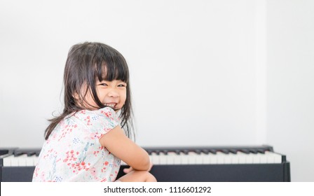 Beautiful little asian girl playing piano in living room or music school.Kindergarten child having fun with learning to play music instrument.Education, skills concept.