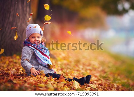 beautiful little baby girl sitting in fallen leaves at autumn park