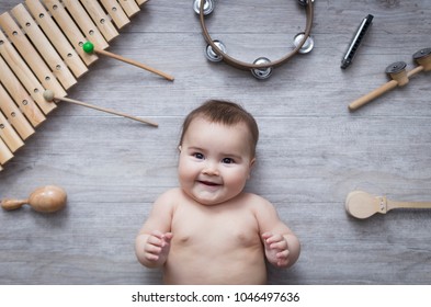 beautiful little baby surrounded by several instruments on a wooden grey floor