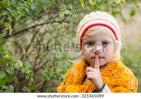 beautiful little blond girl in cap making silence geture, pst.....