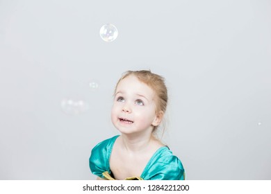 Beautiful little blonde girl, has happy fun cheerful smiling face, pink dress, soap bubble blower. Portrait with pink and white balloons happy