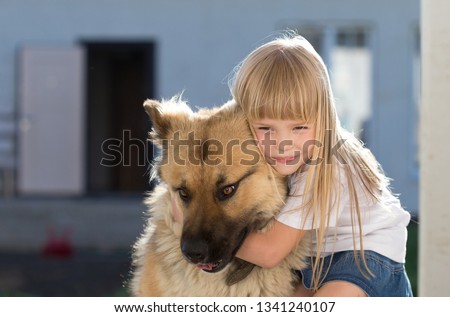 Beautiful little blonde hair girl, has fun smile face, embraces and plays with puppy dog, dressed in  white t-shirt. Child and animals portrait. Happy amazing couple. Kids family look. Close up.