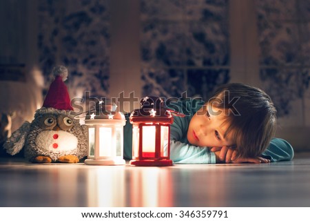 Beautiful little boy, lying down on the floor, looking at candles, making wishes for Christmas