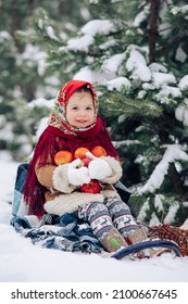 Beautiful little child girl plays with apples during the walk in snowy forest. She dressed in the old Russian style in red headscarf.