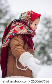 Beautiful little child girl walks in snowy forest. She dressed in the old Russian style in red headscarf. Closeup.