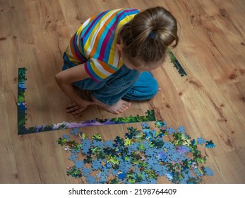 A Beautiful Little Girl Assembles A Complex Puzzle On A Wooden Floor.