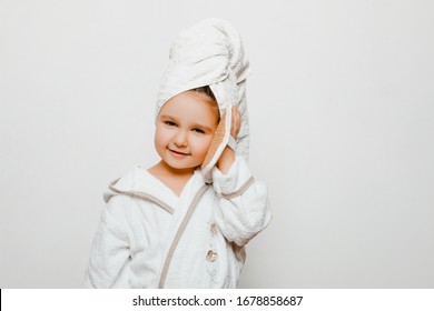 Beautiful Little Girl In Bathrobe And Towel On Head Looking At The Camera With A Smile On Her Face. Child With A Washcloth In His Hands. Washing Hands And Body, Hygiene     