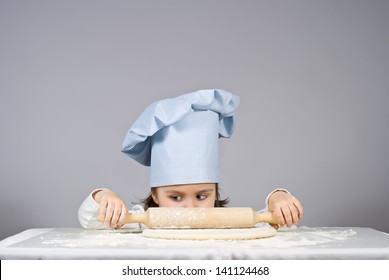 Beautiful little girl cooking pizza over gray background