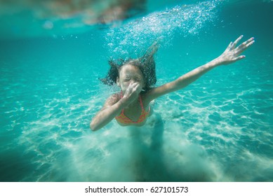 Beautiful Little Girl Diving Underwater In The Sea. She Is Holding Her Nose With Hand And Holding Breat.