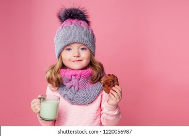 Beautiful Little Girl Drinks Milk And Eats Cookies In A Knitted Hat And Scarf On A Pink Background In The Studio,christmas Night