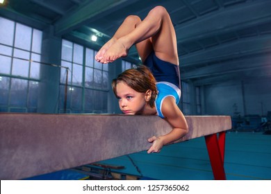 The beautiful little girl is engaged in sports gymnastics on a log at gym. The performance, sport, acrobat, acrobatic, exercise, training concept - Powered by Shutterstock