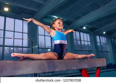 The beautiful little girl is engaged in sports gymnastics on a log at gym. The performance, sport, acrobat, acrobatic, exercise, training concept - Powered by Shutterstock