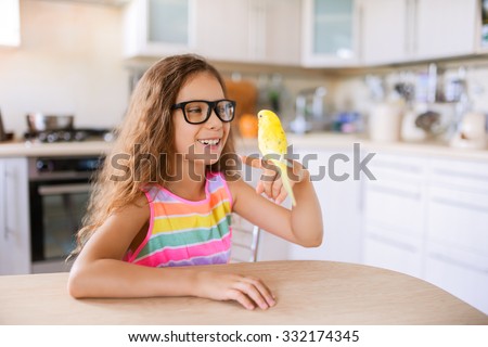 Beautiful little girl with glasses holding the finger yellow wavy parrot.
