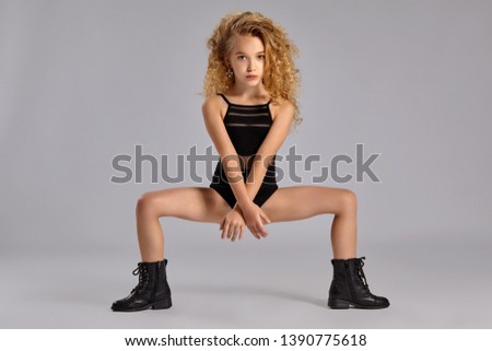 Beautiful little girl gymnast in a black sports swimsuit and boots on a gray background.