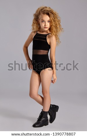 Beautiful little girl gymnast in a black sports swimsuit and boots on a gray background.