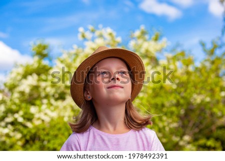A beautiful little girl in a hat looks at the sky. A child in a blooming garden.