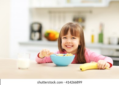 Beautiful little girl having breakfast with cereal, milk and banana in kitchen