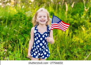 Beautiful little girl with long curly blond hair with american flag in her hand laughing on sunny day in summer park. Independence Day, Flag Day concept - Powered by Shutterstock