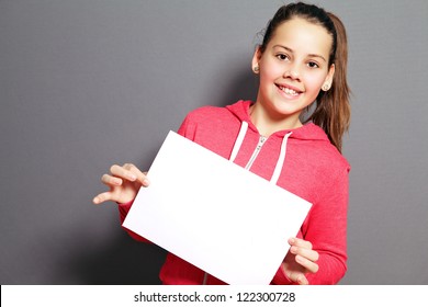 Beautiful Little Girl With A Lovely Smile Holding Up A Blank Sheet Of Paper At A Tilted Angle In Her Hands