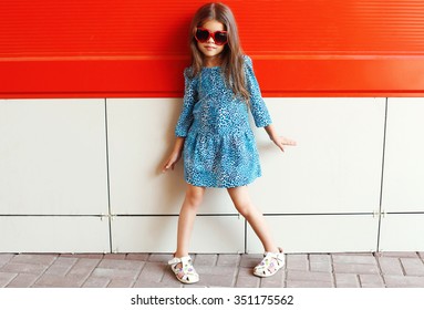 Beautiful little girl model wearing a leopard dress and sunglasses over colorful red background